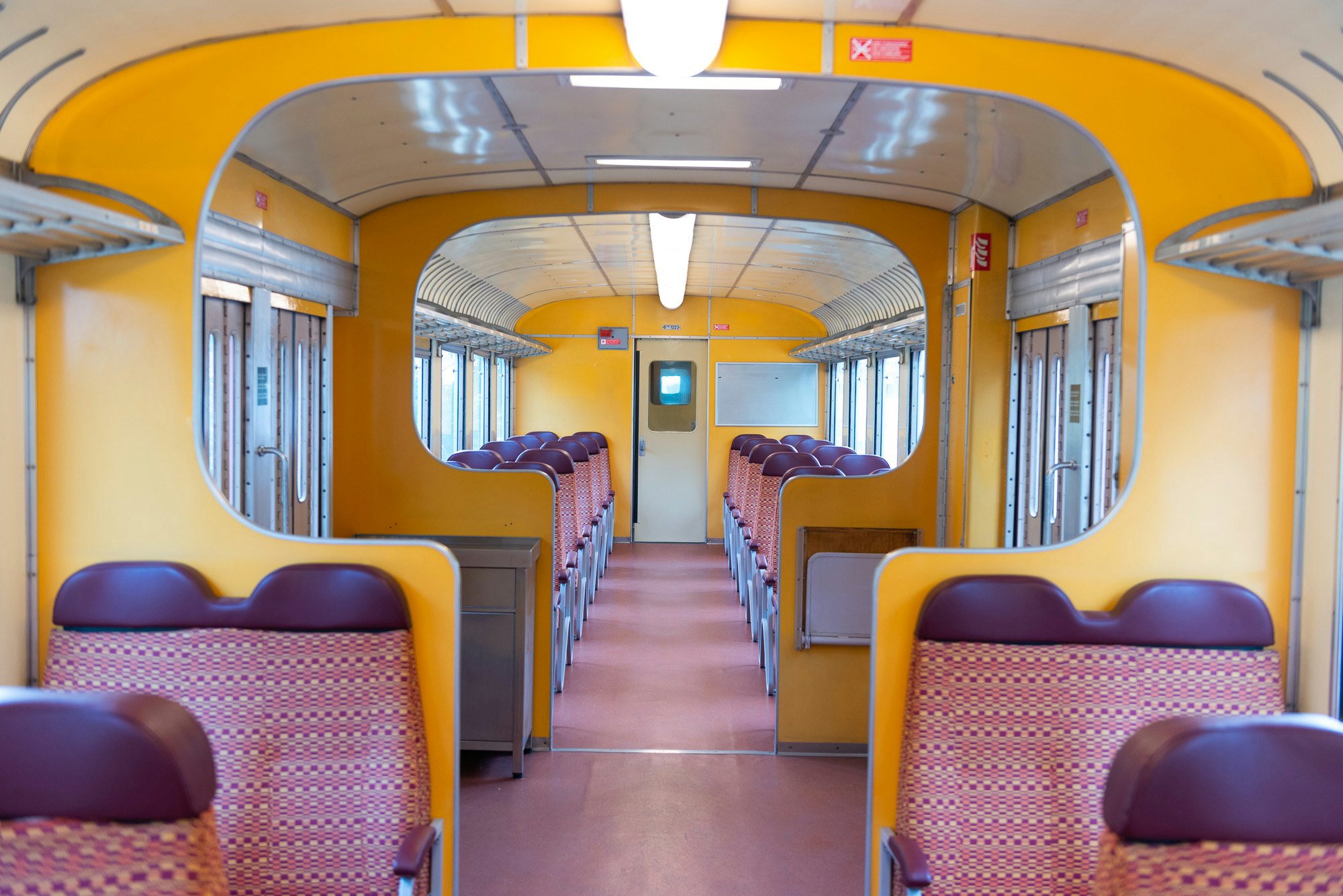 An empty train interior with purple patterned seats and orange partitions.
