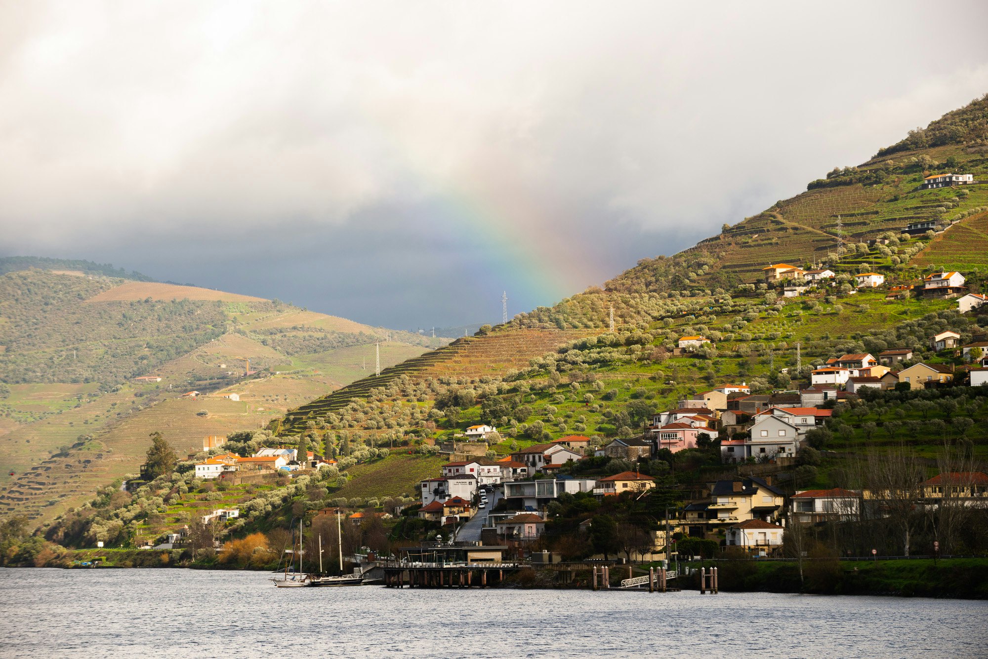 A rainbow over a riverside village and terraced vineyards
