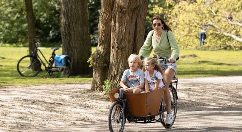 Young woman cycles with her cargo bike with children through the Vondelpark in Amsterdam