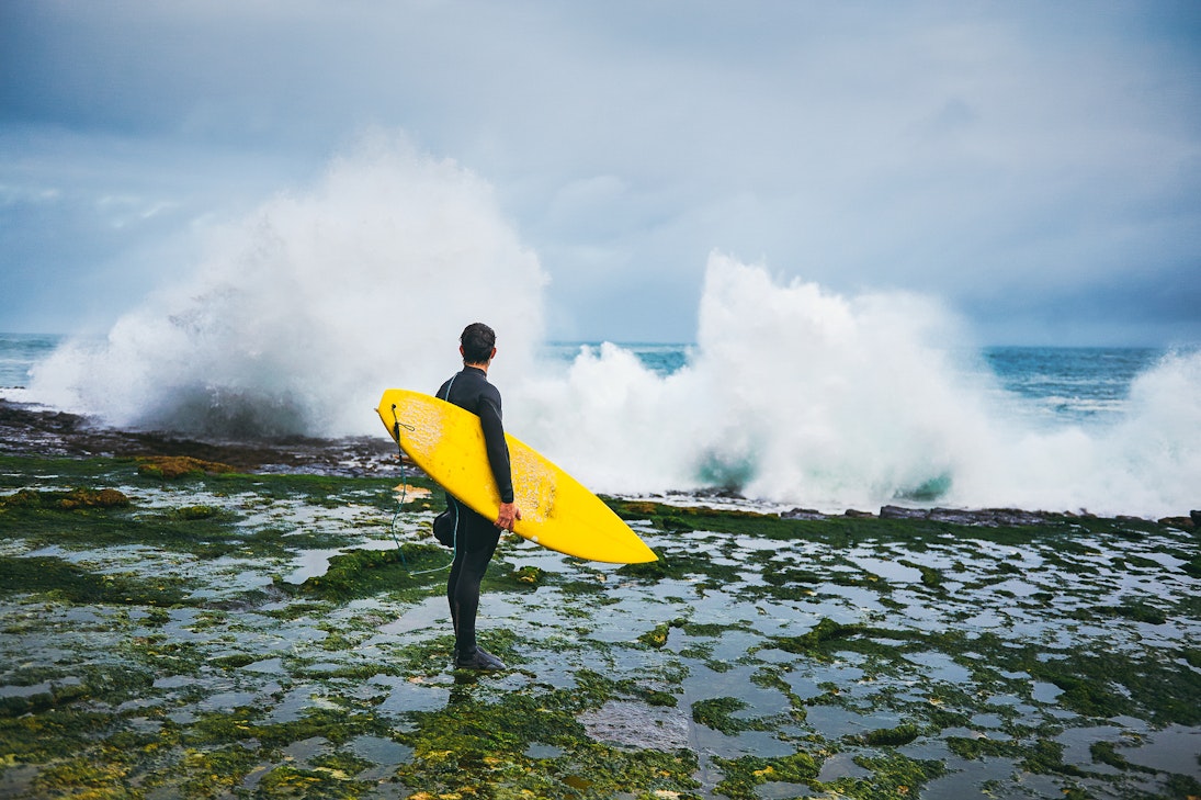 Surfer looking at the waves crushing on the cliff during winter surfing session